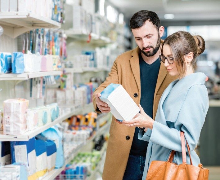 Two shoppers reading a health supplement pack in a pharmacy aisle