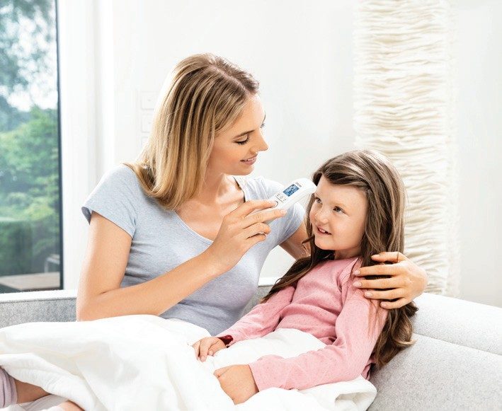 A mother checking her daughter's temperature with a digital thermometer